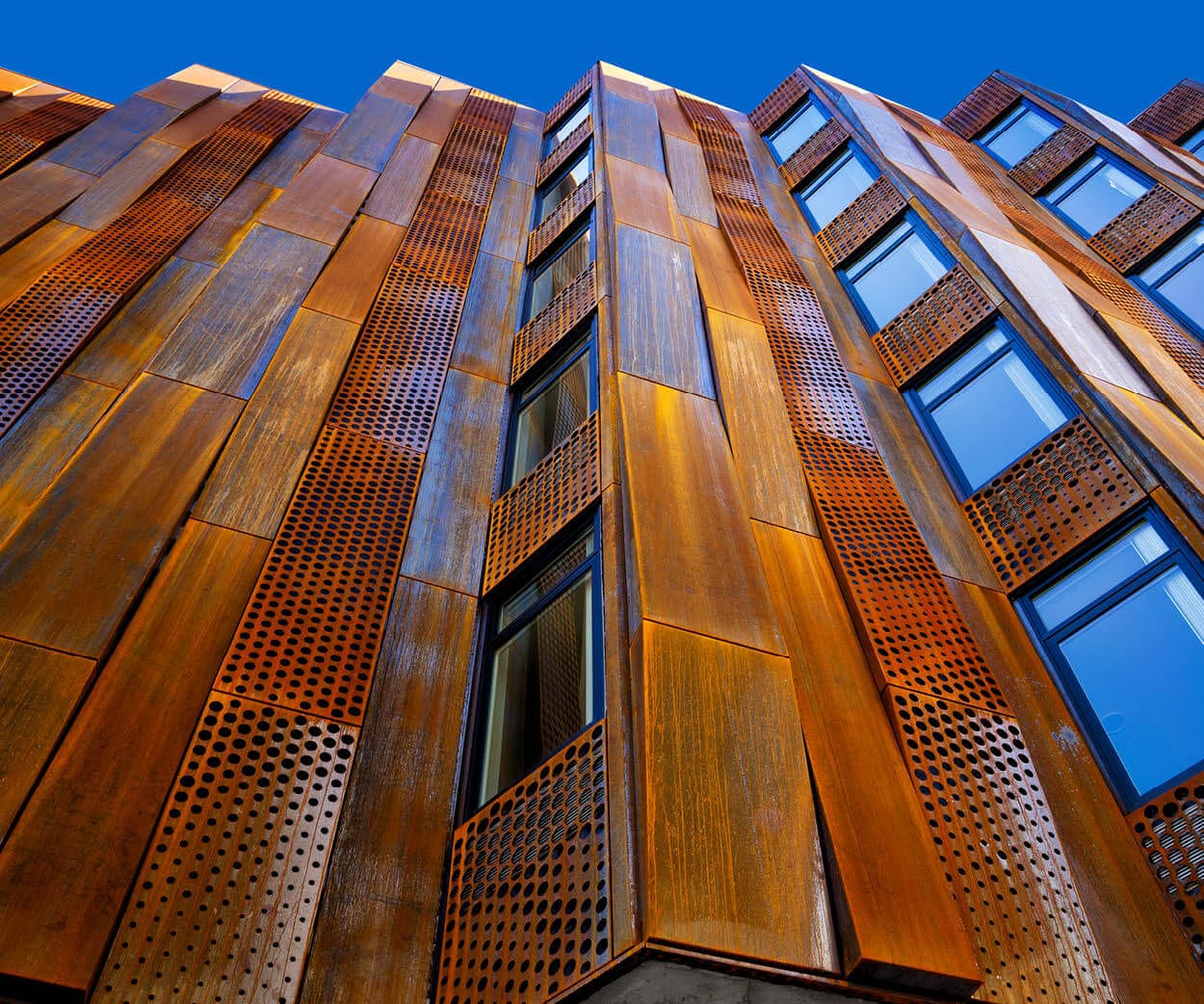 Weathering-steel perforated facade panels on a commercial building against a blue sky